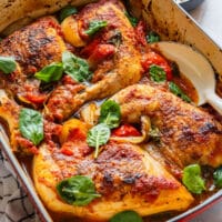 Baked chicken leg quarters in tomato sauce with bell pepper, onion and spinach in a casserole dish.