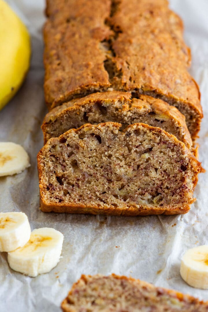 Sliced simple banana bread loaf on parchment paper with banana slices.