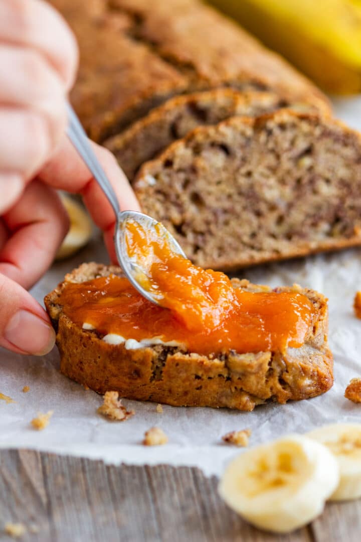 Spreading orange jam over a buttered slice of banana loaf.