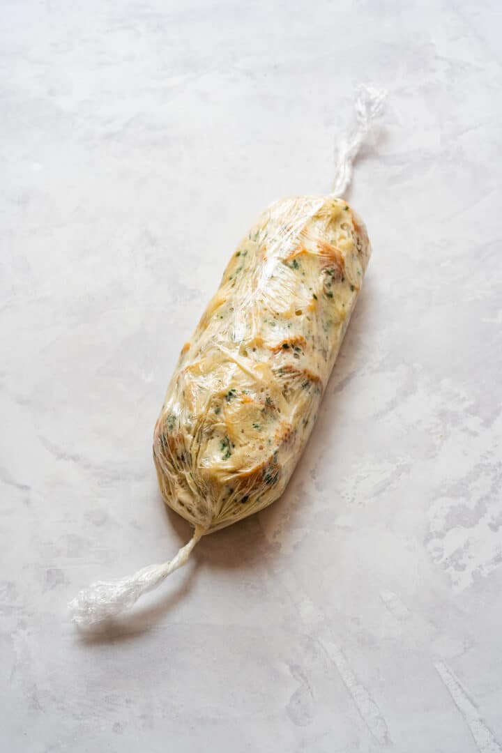 Uncooked bread dumpling log wrapped in plastic wrap and ready for boiling.