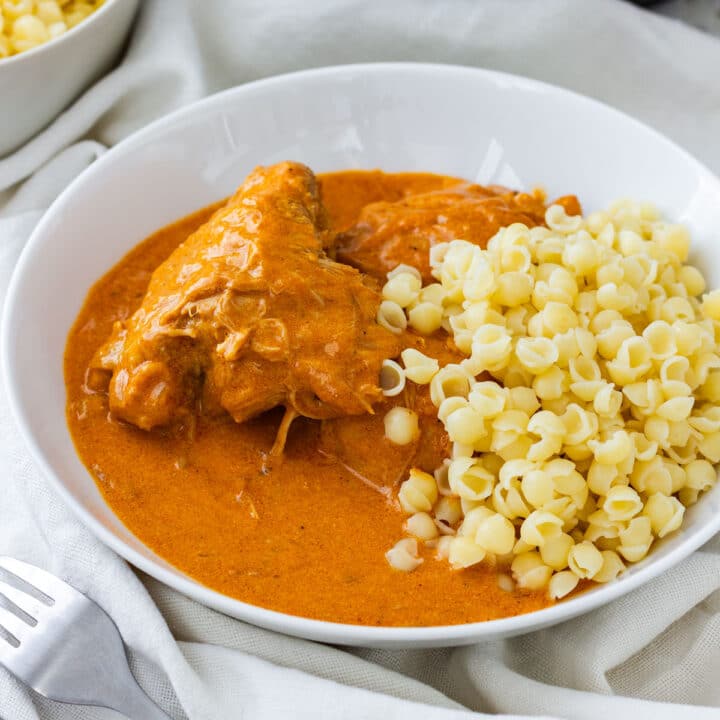Chicken paprikash in a white bowl with pasta shells and creamy paprika sauce.