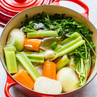 Close-up of a Dutch oven packed with onions, carrots, celery, bay leaf and parsley for vegetable stock.