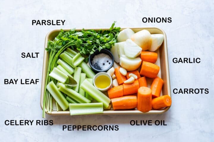 Vegetable stock ingredients on a tray: onions, carrots, celery, garlic, parsley and seasonings.