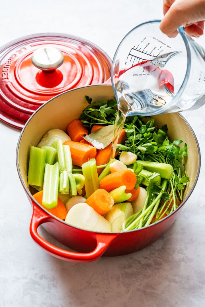Pouring water into a pot with vegetables and herbs for homemade veggie stock.