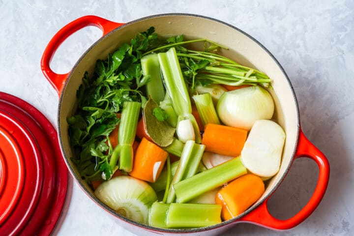 Stock ingredients in a Dutch oven before simmering, with parsley, onions, carrots and celery.