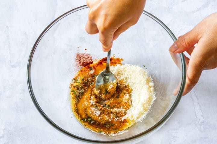 Stirring melted butter with garlic, parmesan and seasonings in a glass mixing bowl.