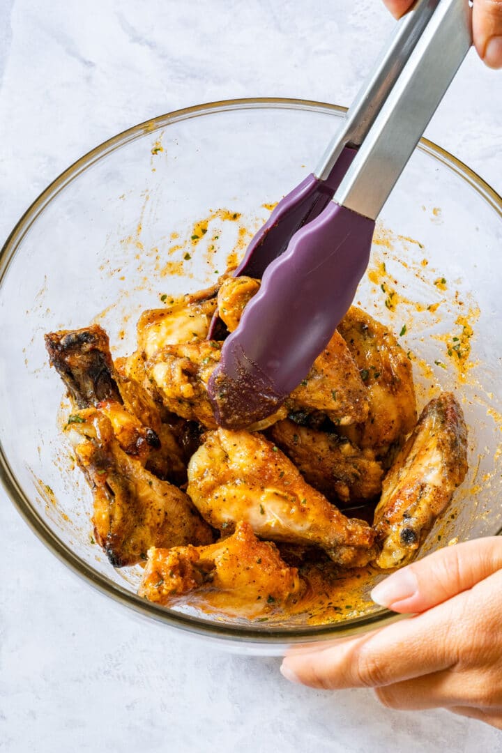 Tossing baked wings in buttery garlic parmesan sauce with kitchen tongs.
