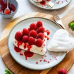 Heart-shaped mini pavlovas with whipped cream, fresh raspberries and raspberry coulis on plates.