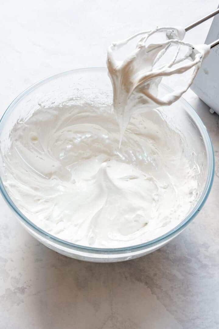 Glossy Swiss meringue whipped to thick peaks in a mixing bowl.