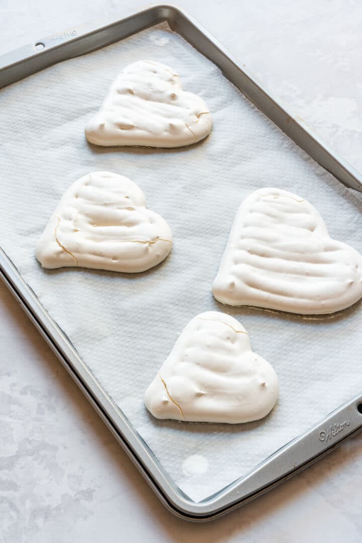Baked meringue hearts cooling on a parchment-lined baking sheet.
