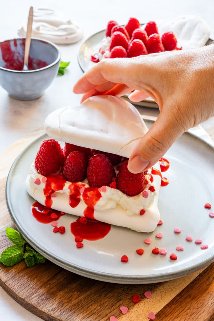 Stacking two meringue hearts with whipped cream and raspberries in the middle.