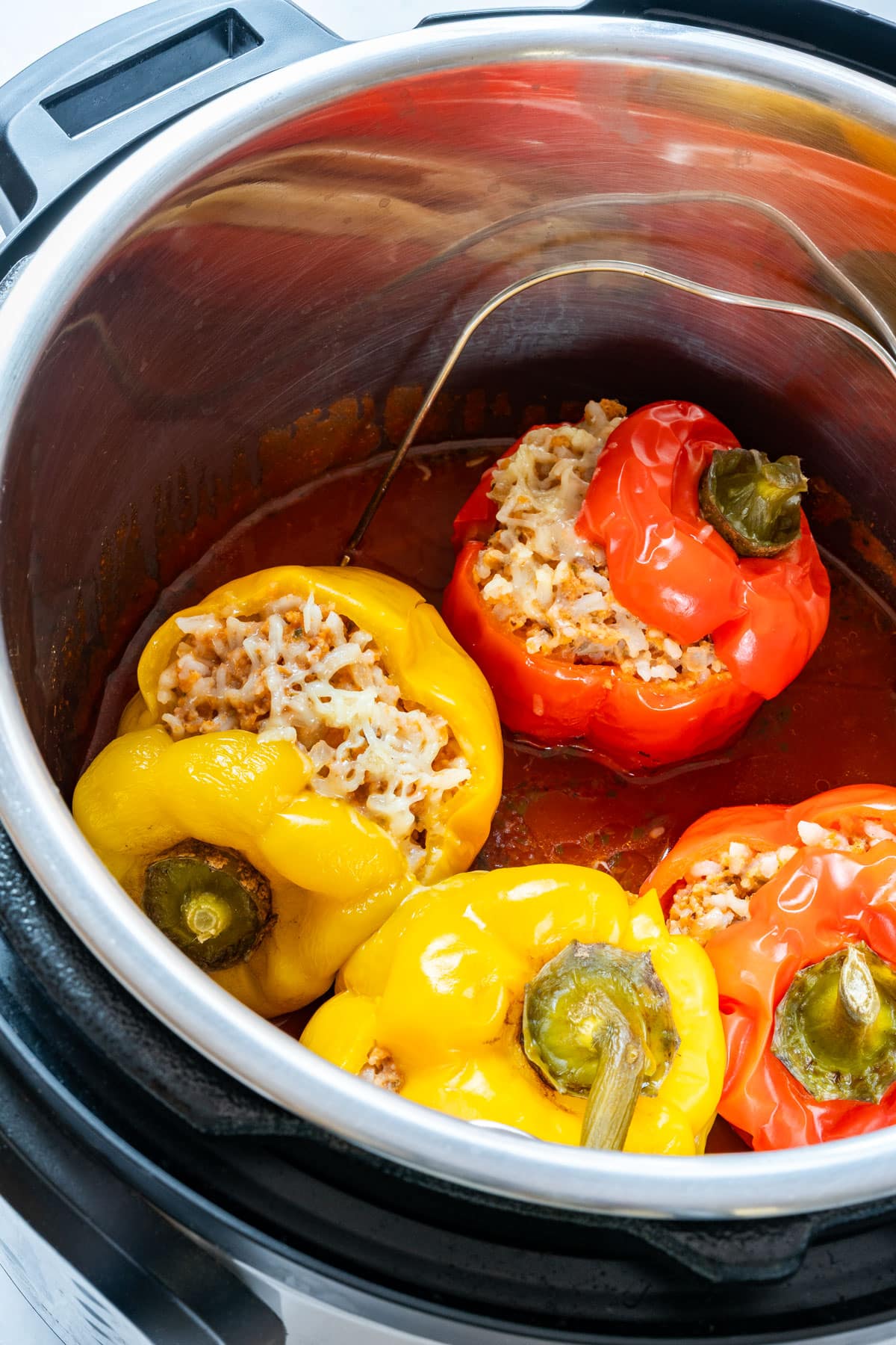 Instant Pot stuffed bell peppers cooking in tomato sauce, topped with melted cheese.