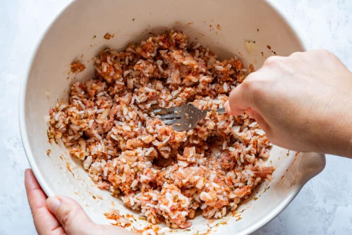 Mixing ground beef and cooked rice filling with seasonings in a bowl.