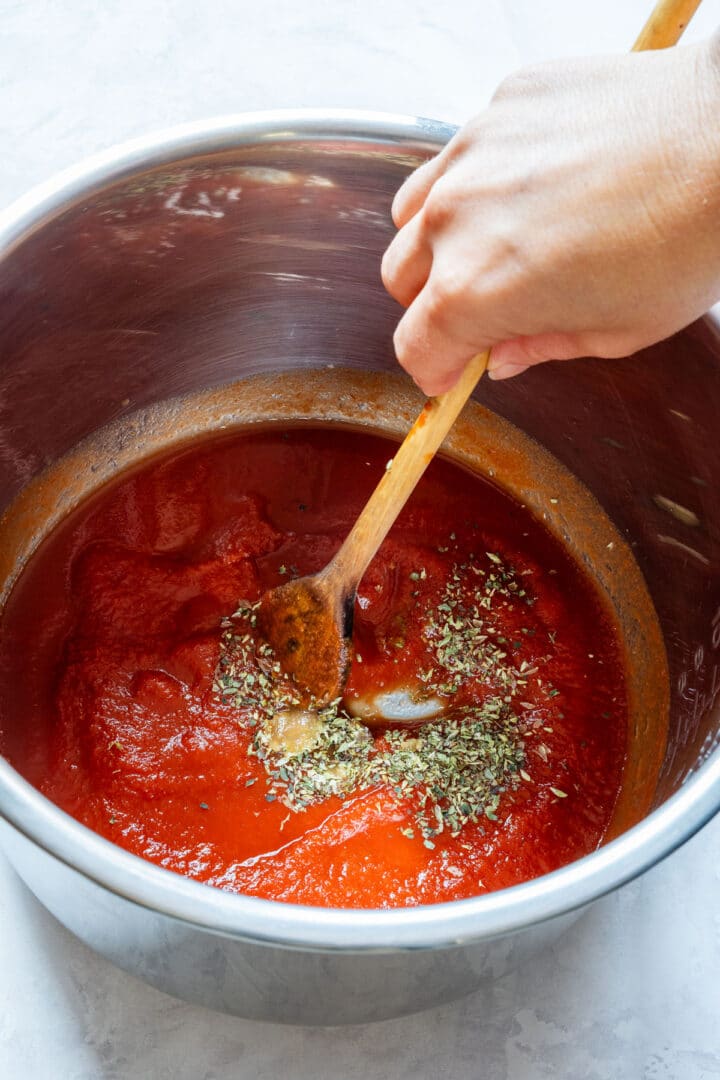 Stirring tomato sauce with herbs and garlic in the Instant Pot insert.