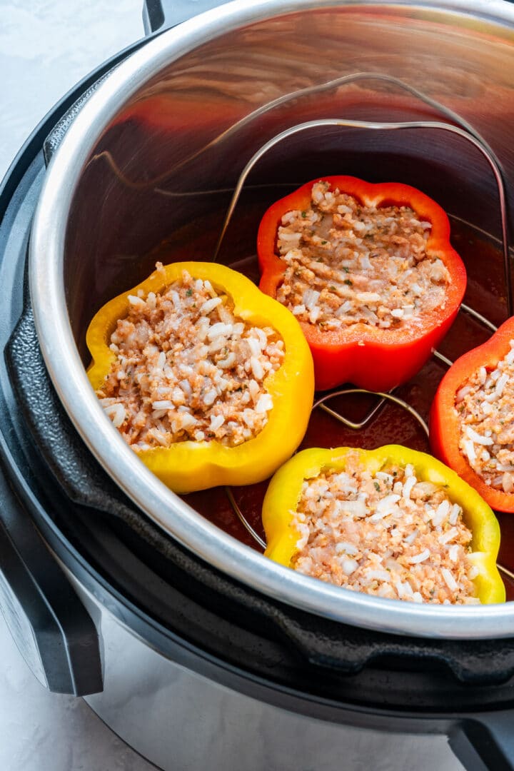Uncooked stuffed bell peppers arranged above tomato sauce in the Instant Pot.