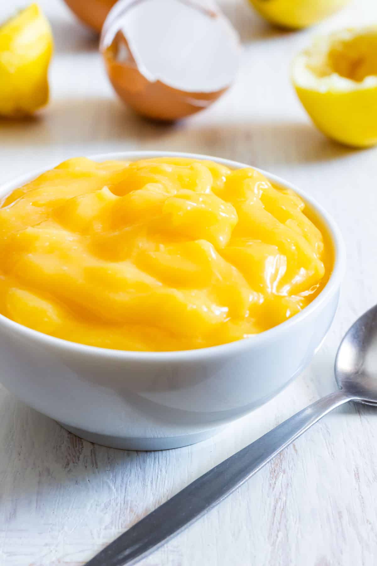 Smooth lemon curd made with whole eggs in a white bowl with a spoon.