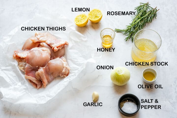 Ingredients laid out for the recipe: chicken thighs, lemon, rosemary, onion, garlic, honey, stock, olive oil, salt and pepper.