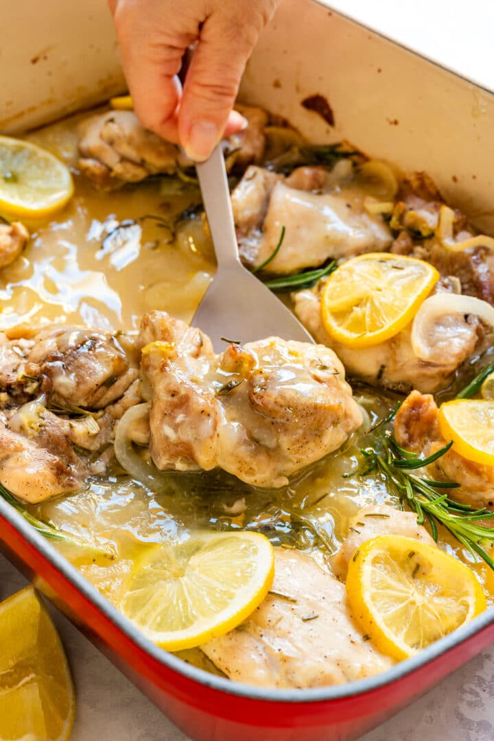 Lifting a cooked chicken thigh from the lemony sauce with a spatula.