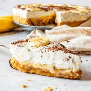 Slice of banoffee pie showing biscuit crust, dulce de leche, banana and whipped cream layers.