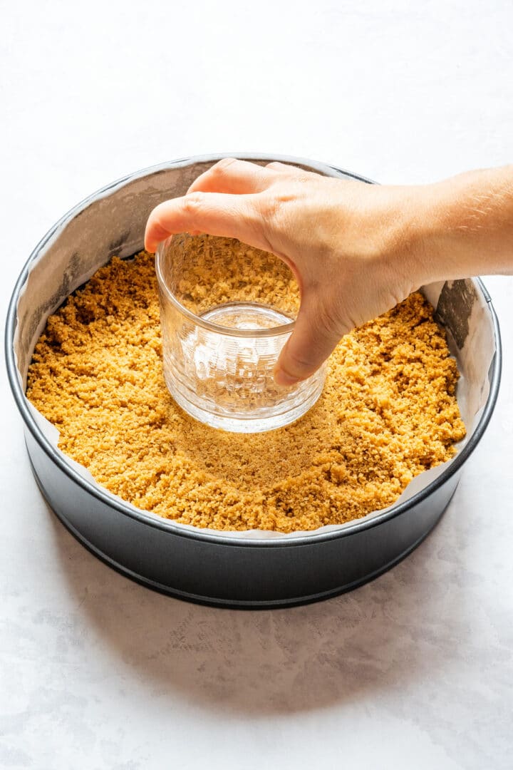Pressing biscuit crumbs into the bottom of a springform pan for the crust.