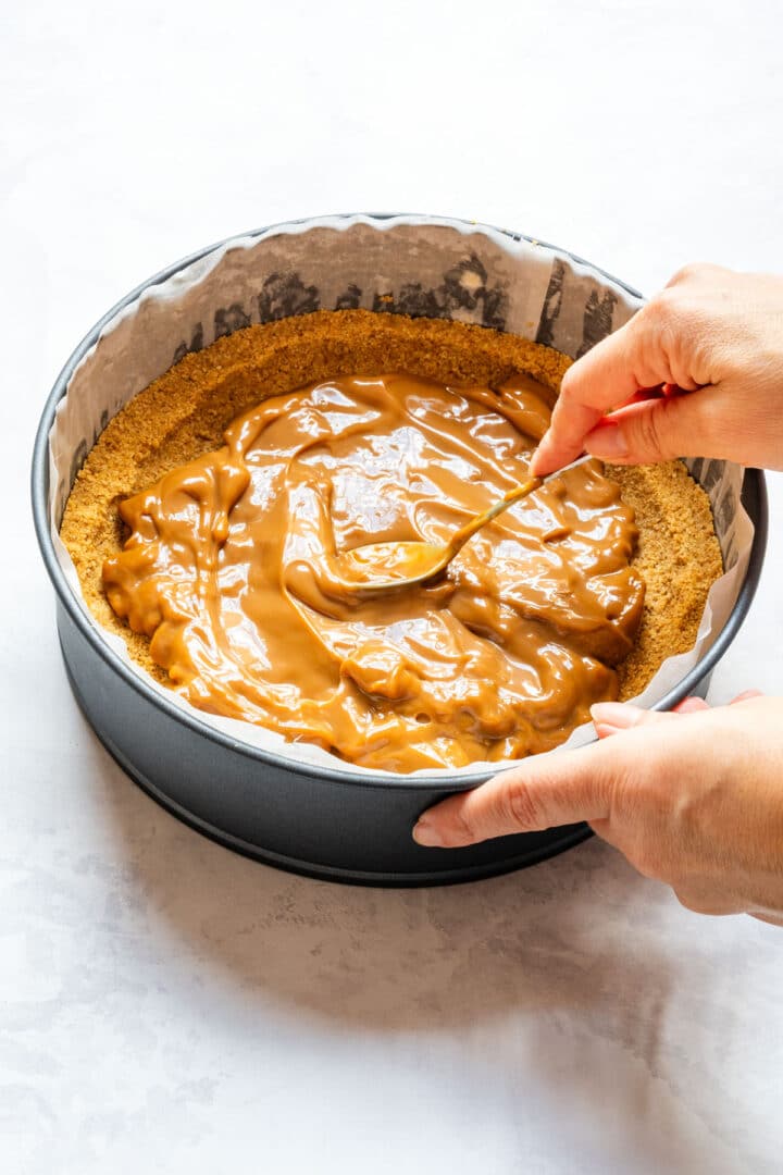 Spreading dulce de leche over the chilled biscuit crust in a springform pan.