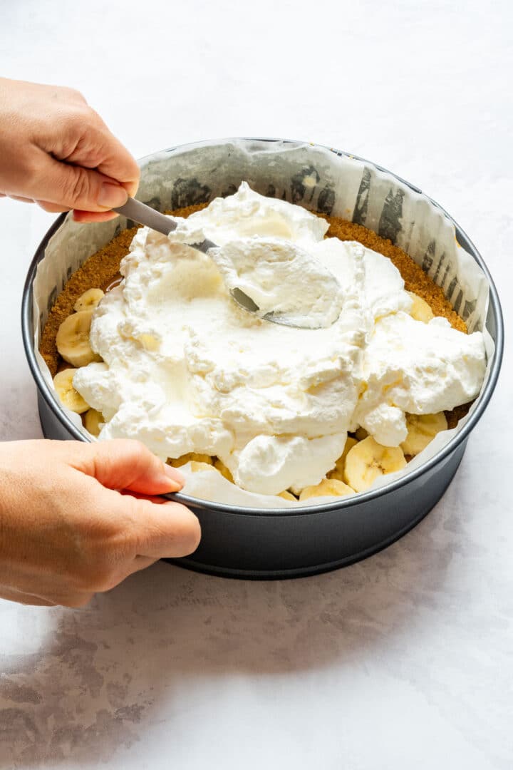 Spreading whipped cream over sliced bananas in the pie pan.