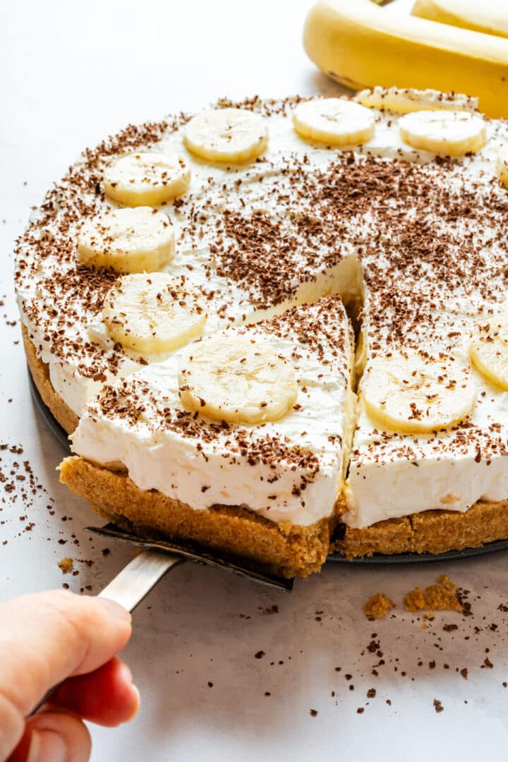 Lifting a slice from the pie with banana slices and grated chocolate on top.