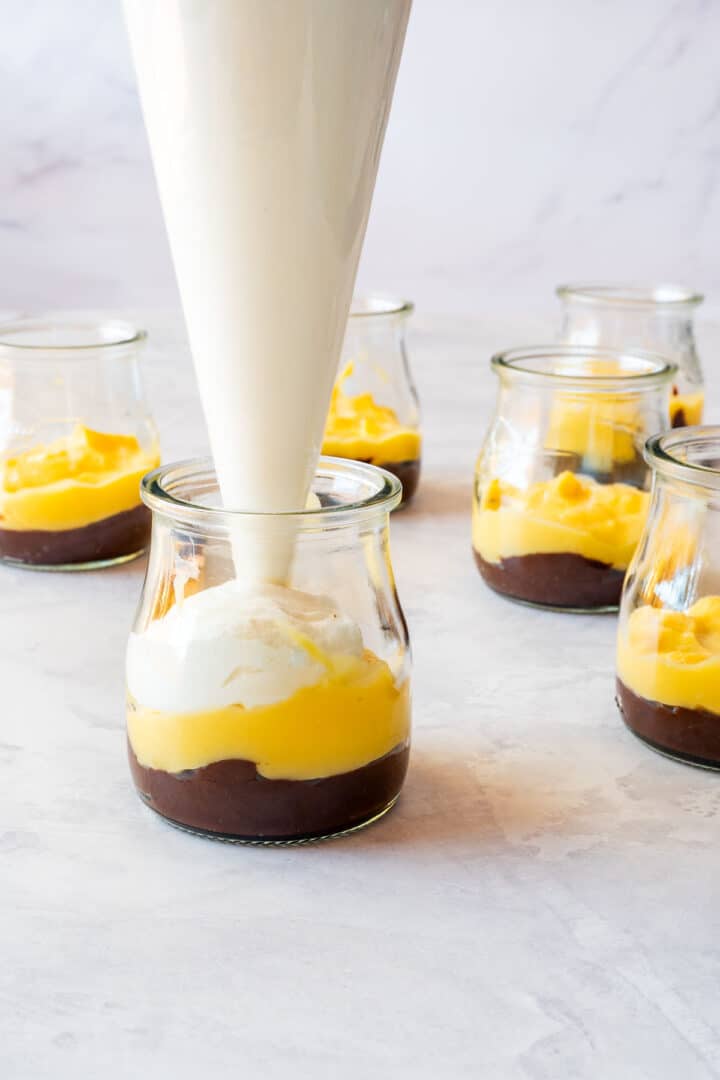 Piping whipped cream onto lemon curd dessert cups in small glasses.