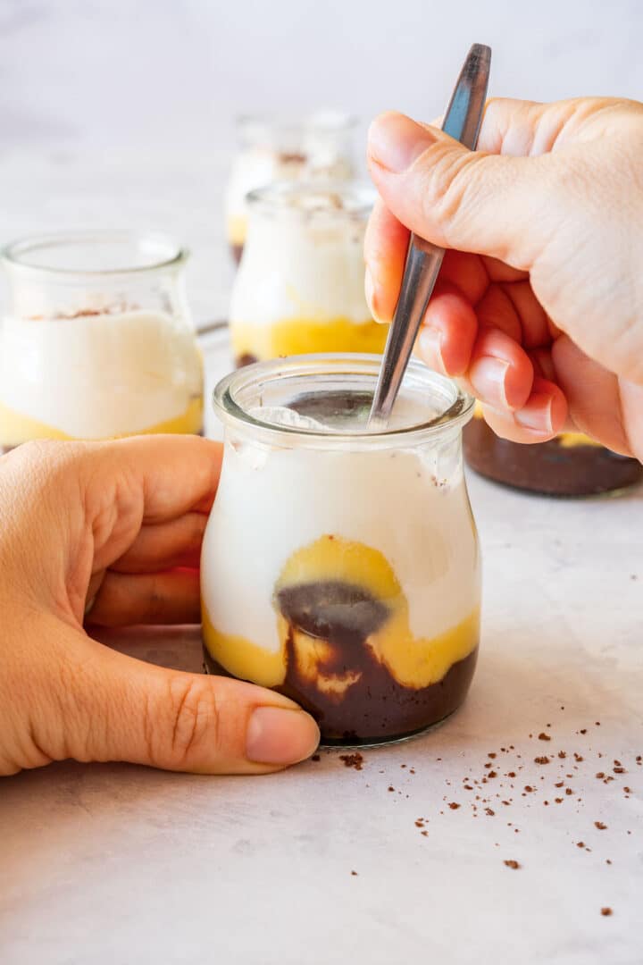 Spoon scooping lemon curd dessert cup, showing chocolate, lemon curd and whipped cream layers.