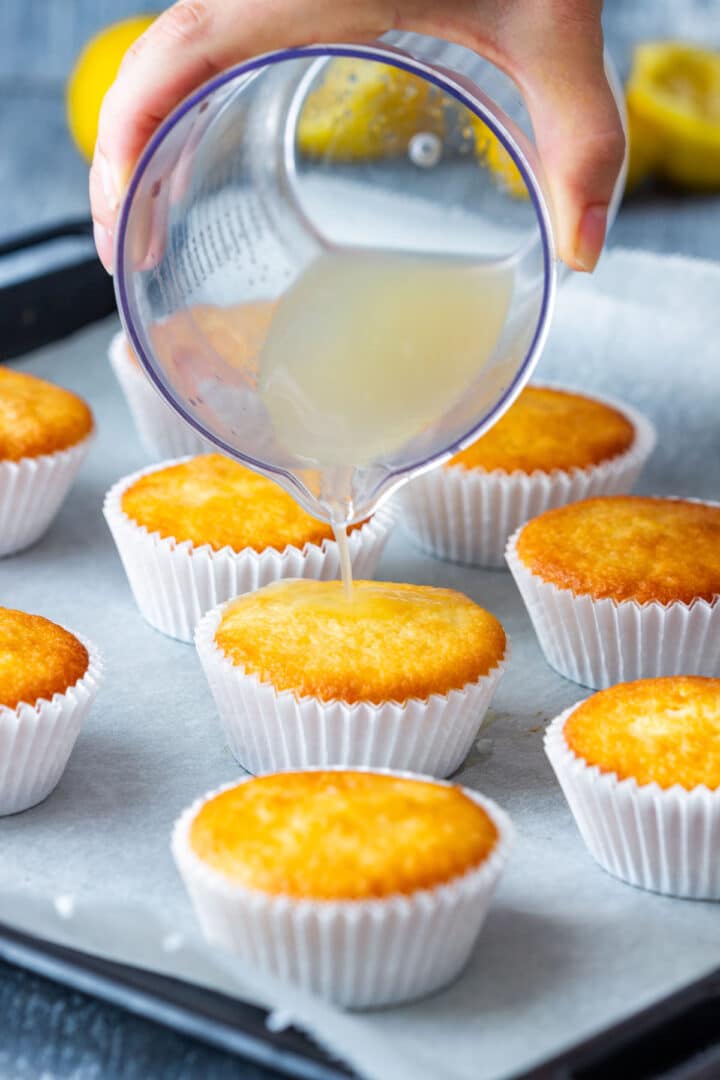 Pouring lemon juice over warm lemon cupcakes after baking.