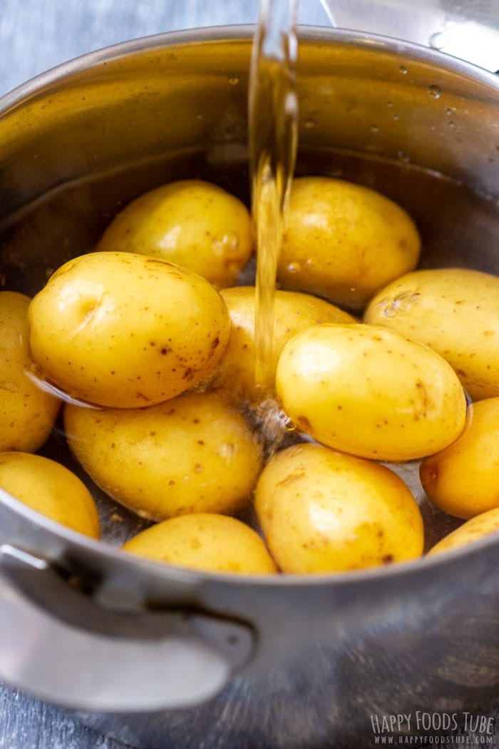Baby potatoes being covered with water in a stainless-steel pot before boiling.
