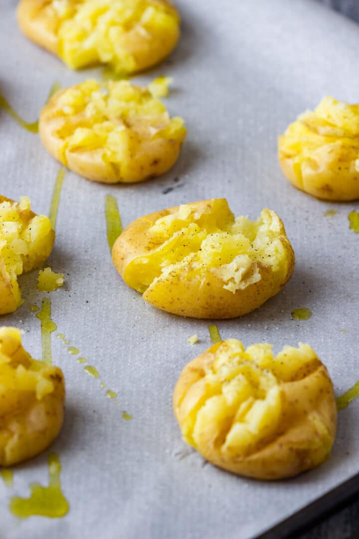 Smashed baby potatoes drizzled with olive oil on a baking sheet before baking.