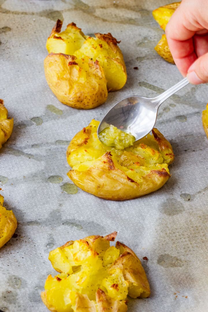 Minced garlic and olive oil being spooned over baked smashed potatoes.