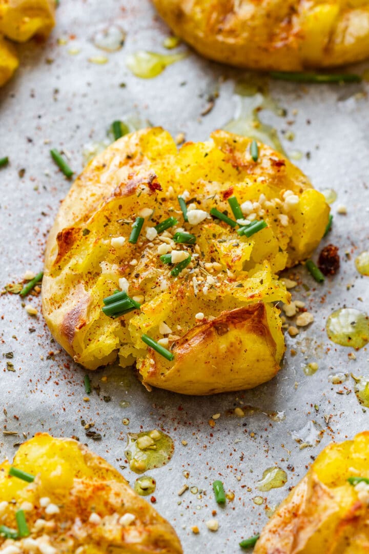 Close-up of a crispy smashed potato with golden edges, chives, paprika and almond topping.