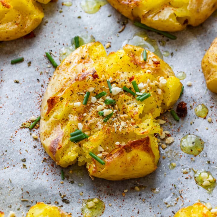 Golden garlic smashed potatoes on parchment paper with herbs, chives and olive oil.