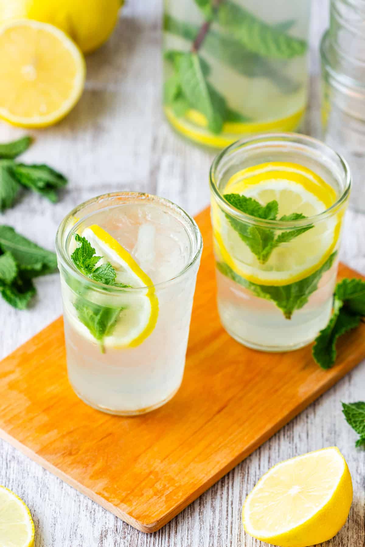 Two glasses of mint lemonade with lemon slices and fresh mint on a wooden board.