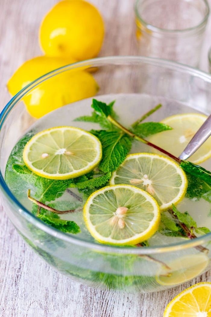Mint lemonade in a glass bowl with floating lemon slices and fresh mint leaves.