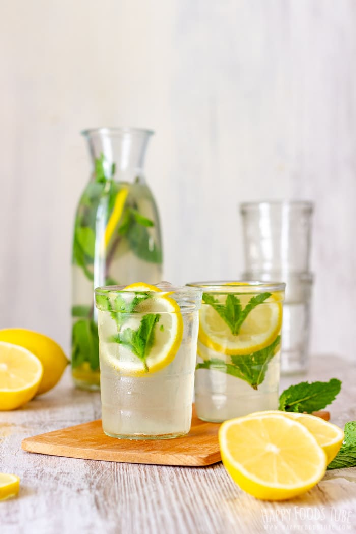A tall carafe of mint lemonade with two filled glasses, lemon slices and fresh mint on a wooden board.