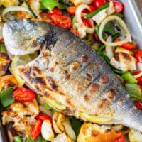 Overhead close-up of grilled whole fish with lemon slices, served on a warm grilled vegetable and bread salad.