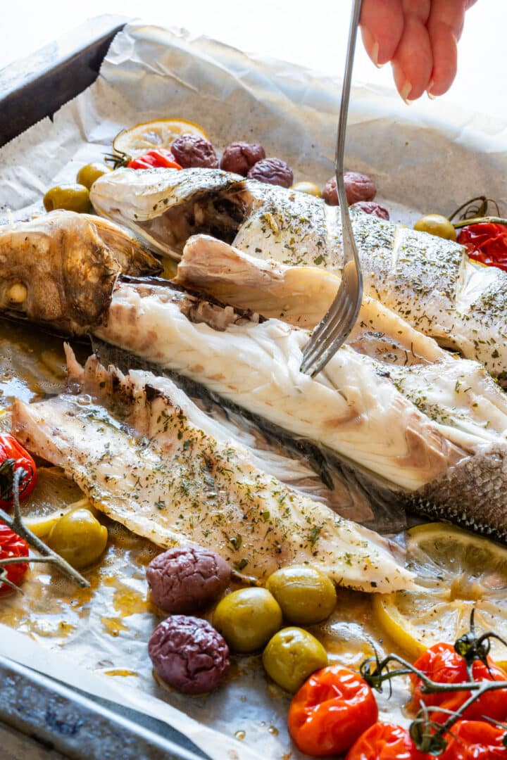 Flaking the tender white flesh of roasted branzino with a fork after baking.