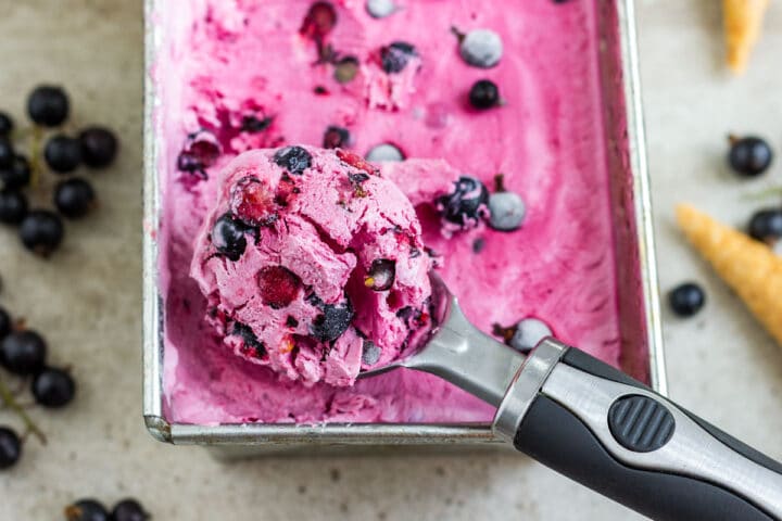 A scoop of finished pink blackcurrant ice cream lifted from the loaf pan with whole berries showing through.