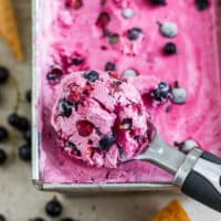 Close-up of a scoop of berry-flecked pink blackcurrant ice cream above the loaf pan.