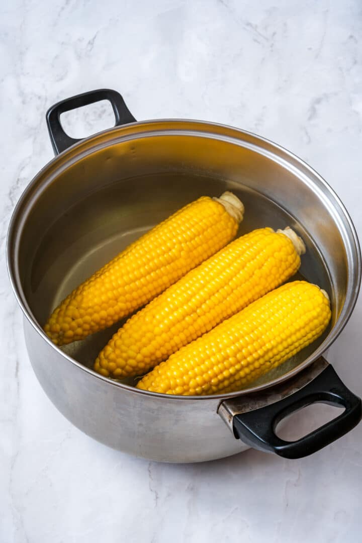 Ears of corn cooking in a large pot of water.