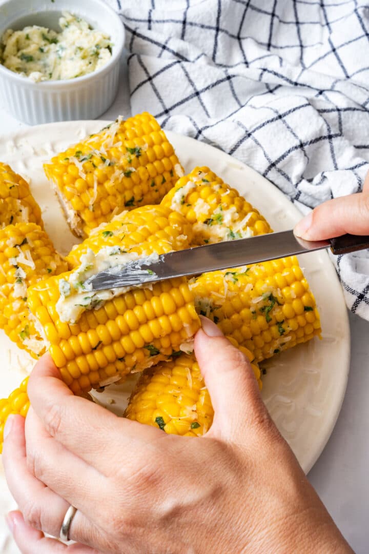 Garlic Parmesan butter spread over a warm piece of corn with a knife.