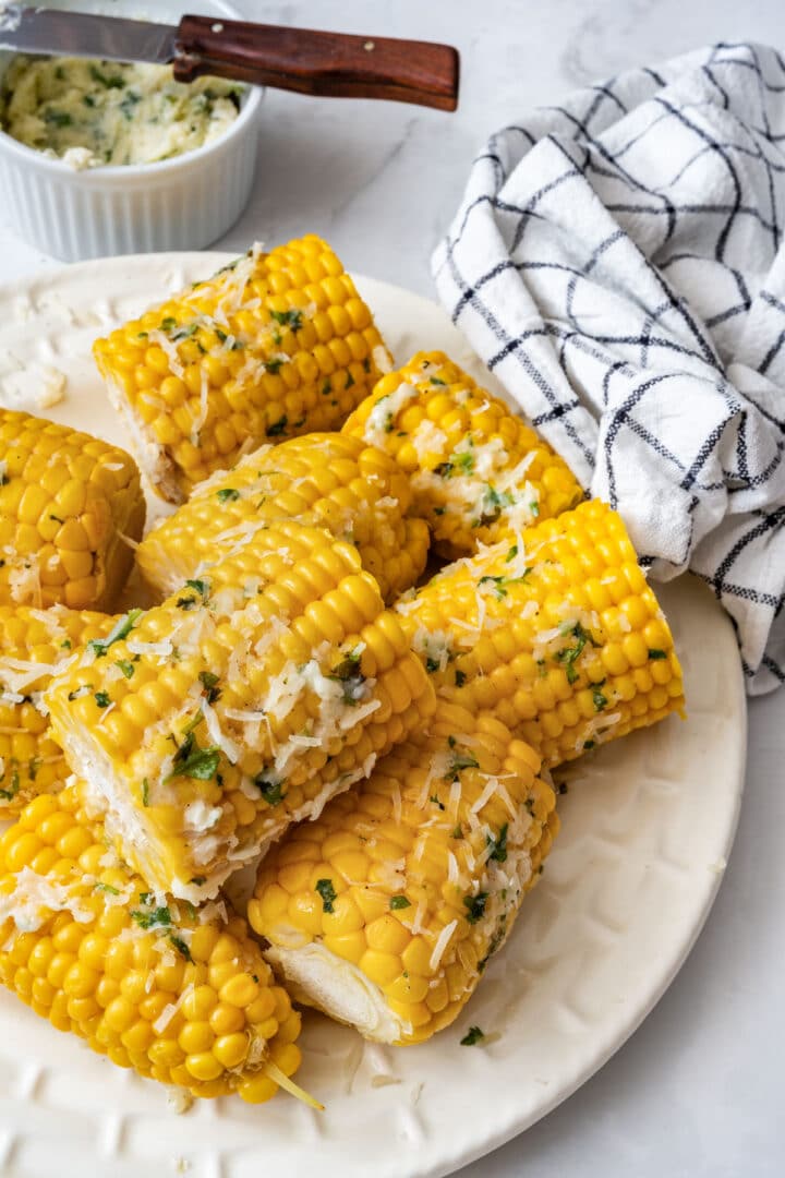 Corn pieces coated with Parmesan butter and cilantro on a white plate.