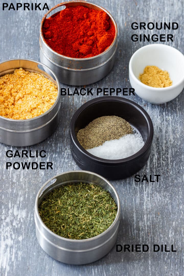 Ingredients for fish seasoning: paprika, garlic powder, black pepper, salt, ground ginger and dried dill in small tins.