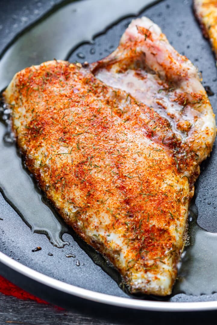 White fish fillet coated in homemade fish seasoning cooking in a pan.