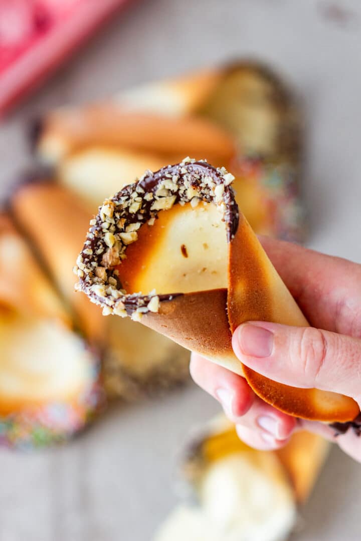 Hand holding a thin baked cone with a chocolate and walnut rim.