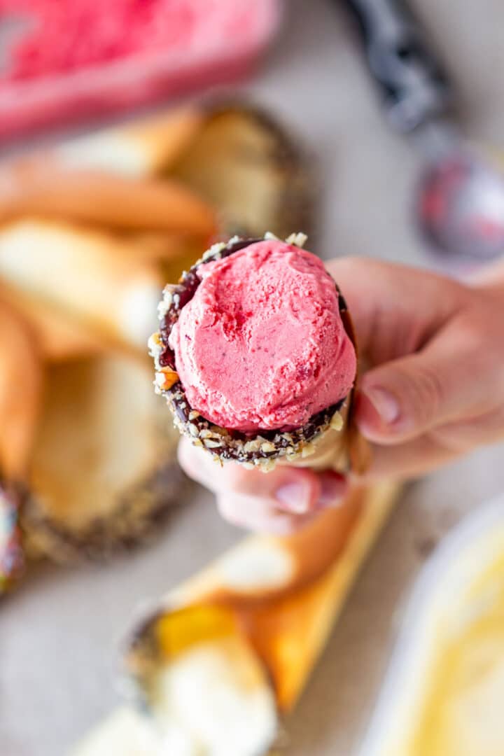 Hand holding a chocolate-dipped cone filled with strawberry ice cream.