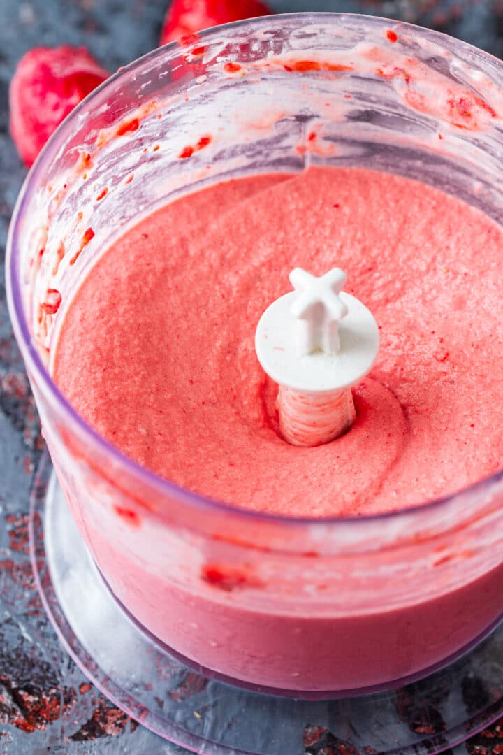 Smooth strawberry ice cream mixture in a food processor bowl.